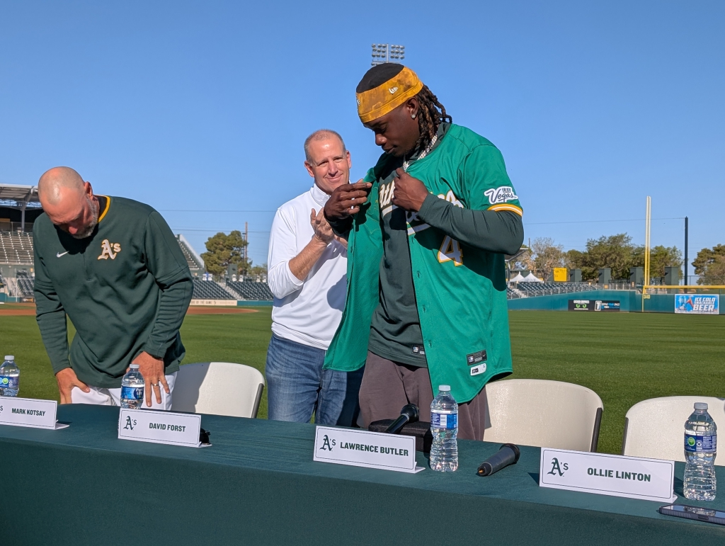 Lawrence Butler putting on an Athletics jersey at the press conference announcing his contract extension